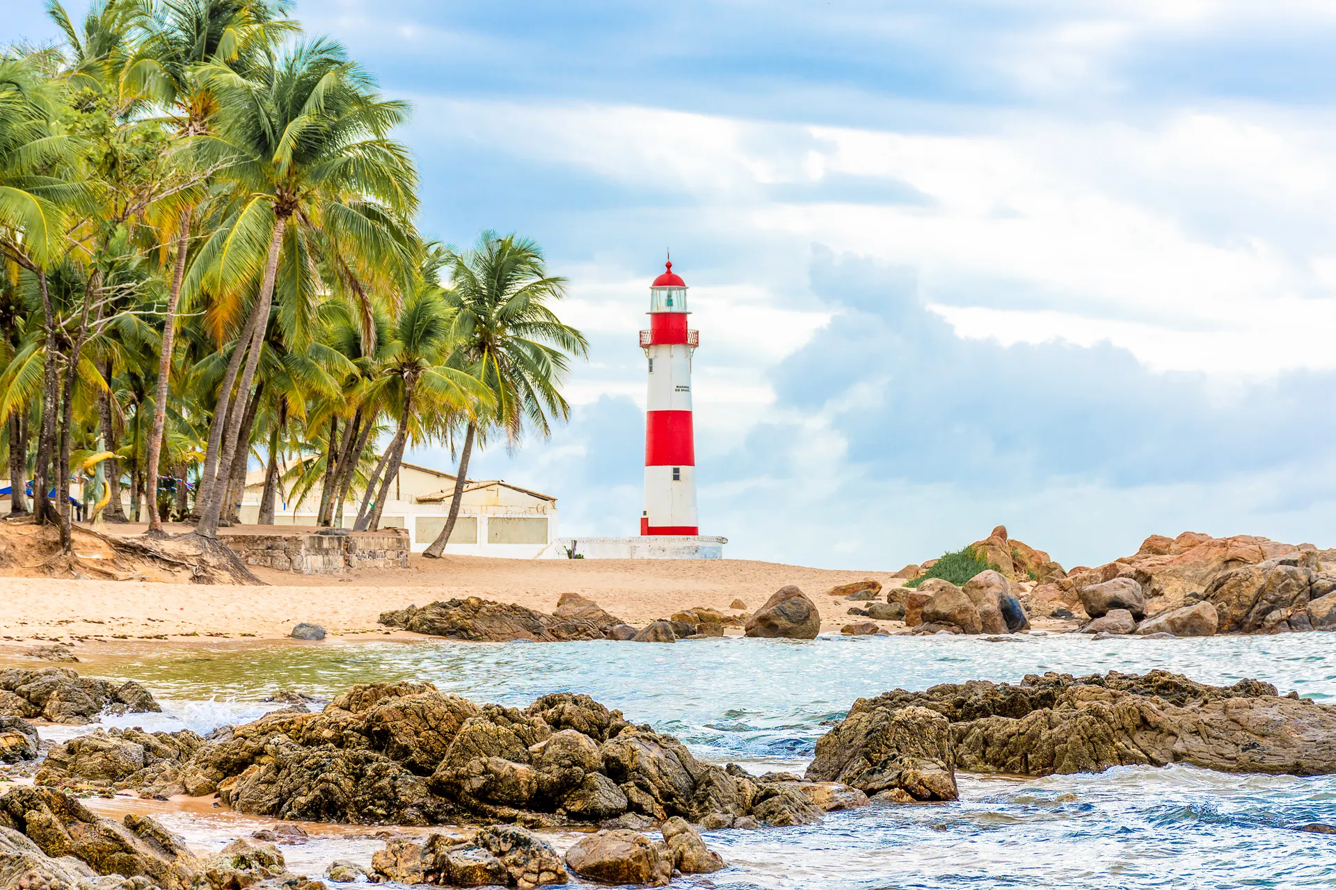 Farol de Itapuã entre coqueiros, pedras e mar — Salvador, Bahia